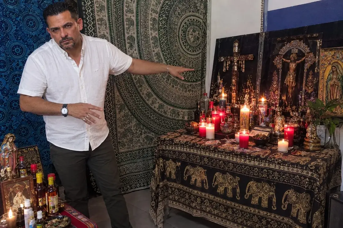 Jairo junto a su altar de consulta, con imágenes religiosas, velas y elementos de protección y limpieza energética