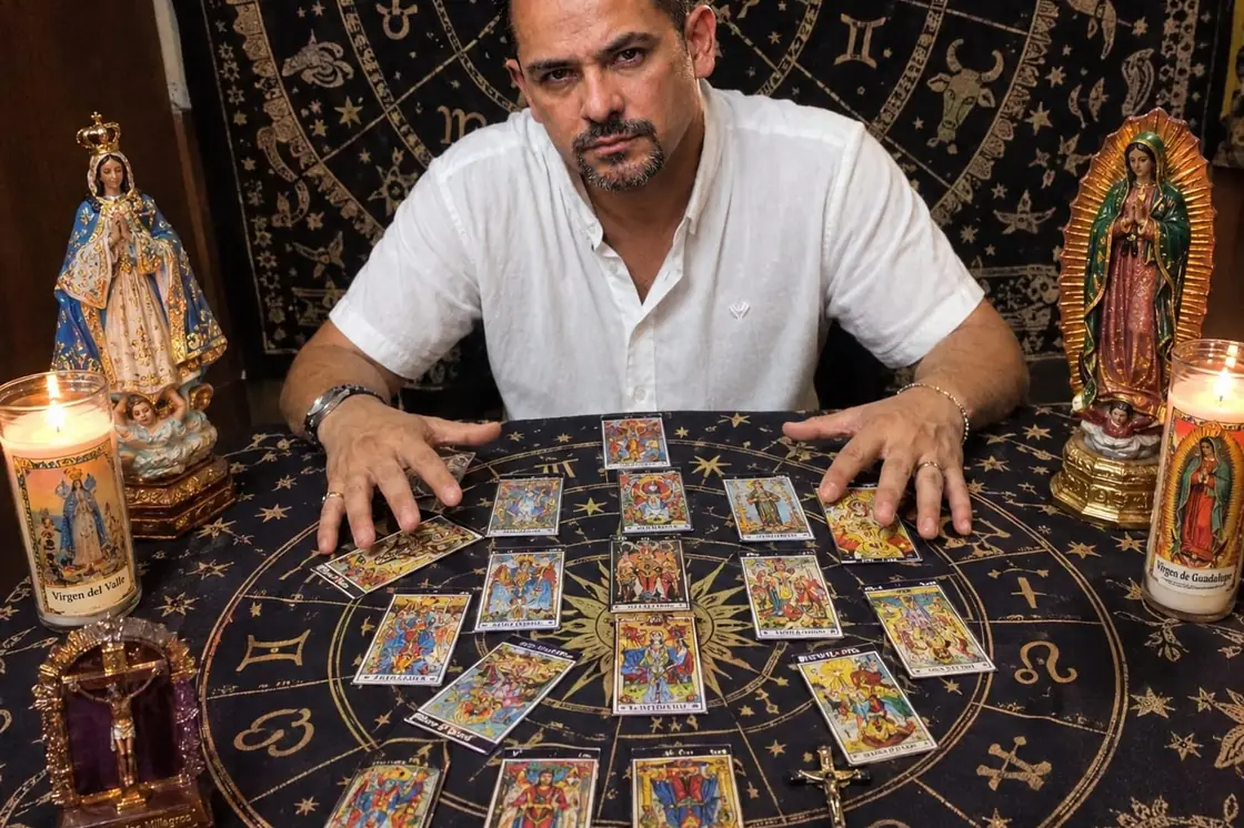 Jairo, tarotista, con las manos sobre una tirada de tarot extendida en círculo sobre el tapete, entre velas encendidas e imágenes religiosas